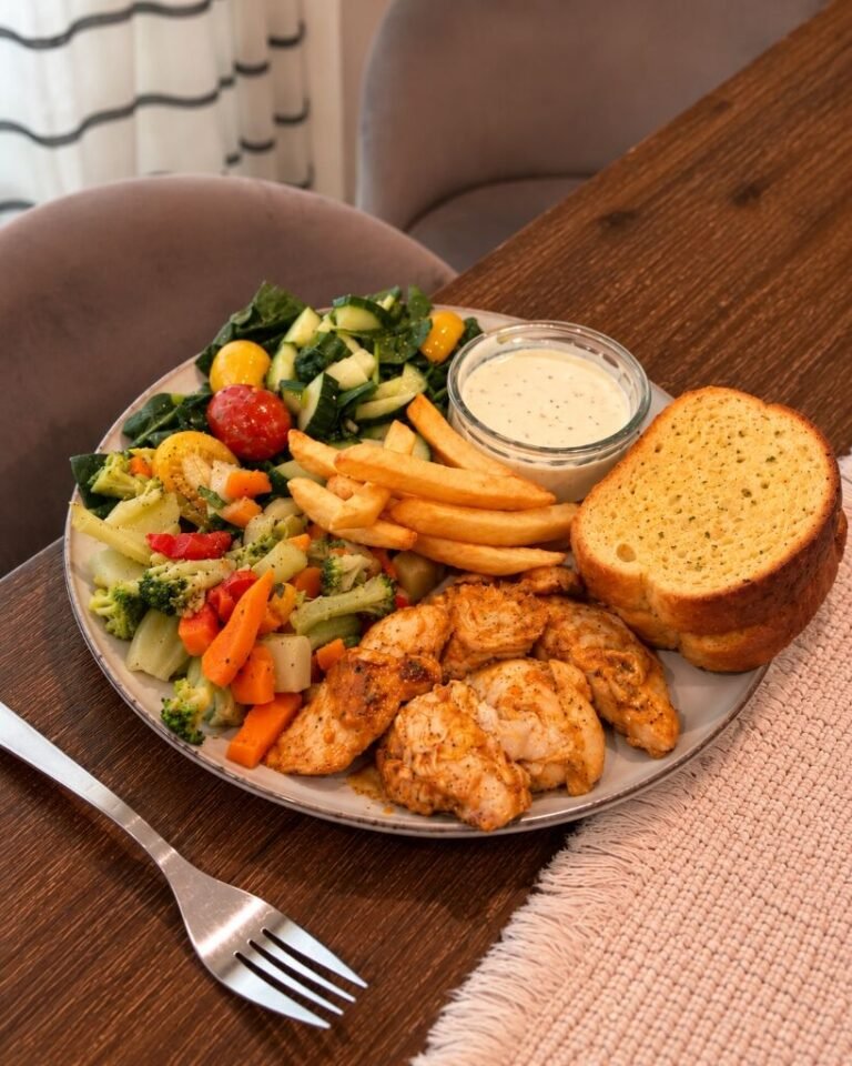 A plate of glazed honey BBQ chicken with warm mixed vegetables, a green salad, fries, garlic bread and a small bowl of lemon-Dijon yogurt sauce